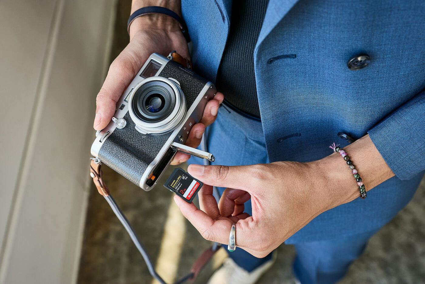 Hands putting an SD card into a silver compact camera